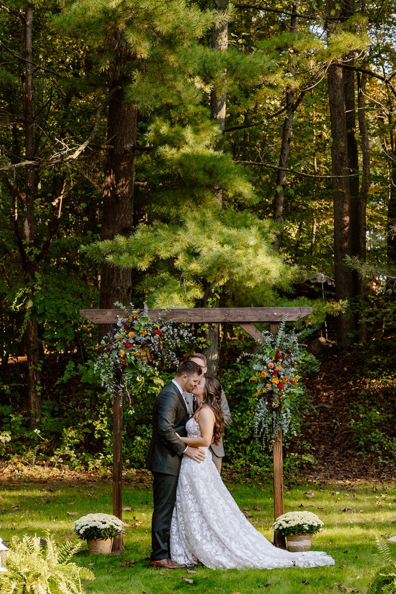 A couple kissing in front of wooden arch at their wedding the woman is wearing a white wedding dress the man is wearing a black suit 