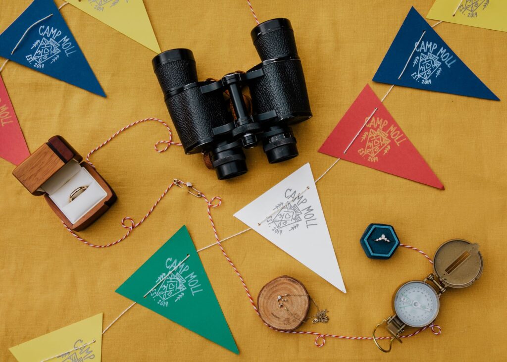 Table decorations including colorful flags, binoculars, a compass and wedding rings on top of an orange tablecloth 