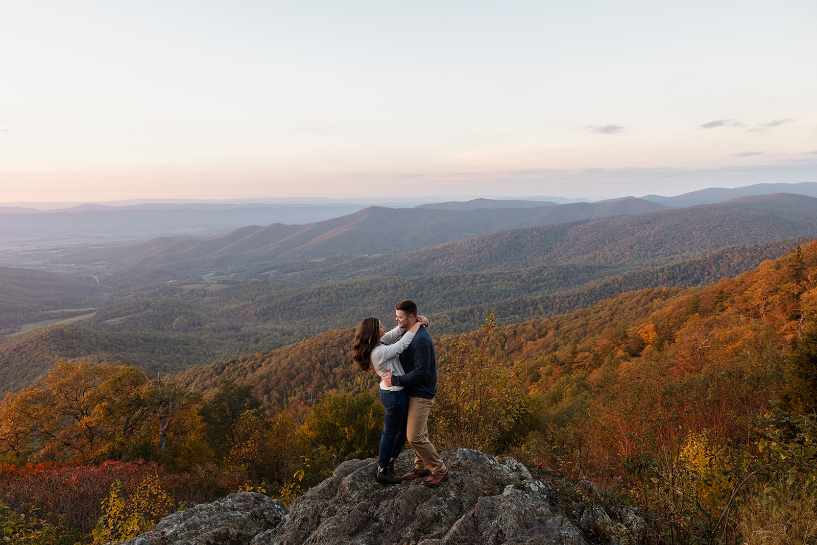 An engaged couple standing facing each other and smiling in front of. some fall foliage during their Shenandoah Adventure Session in fall.