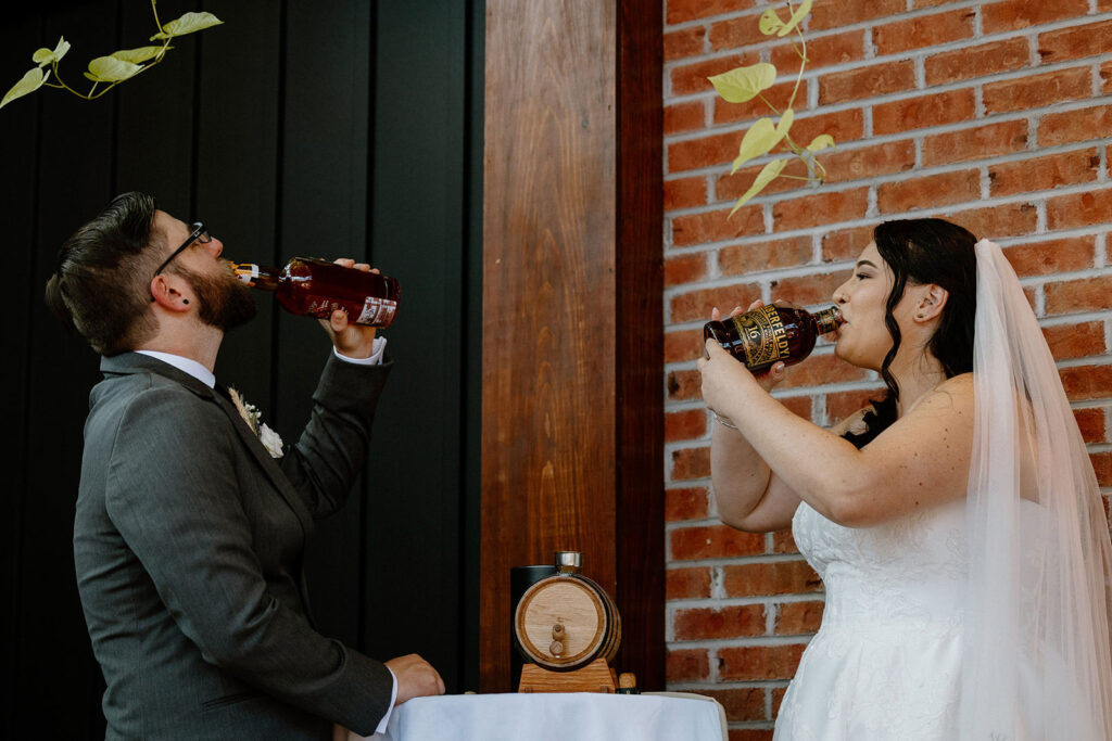 A couple each takes a shot from different whiskey bottles during a whiskey blending ceremony at their elopement