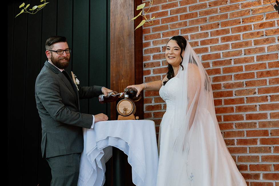 A couple blends two different bottles of whiskey into a barrel during a whiskey blending ceremony at their elopement ceremony