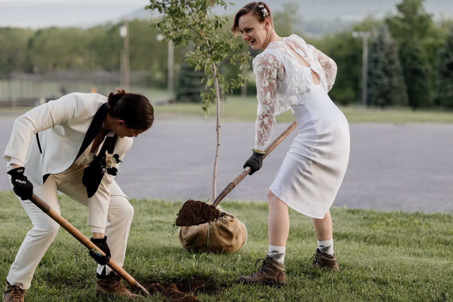 a couple perfomring a tree planting ceremony both are holding shovels and digging a hole in the ground for their tree 