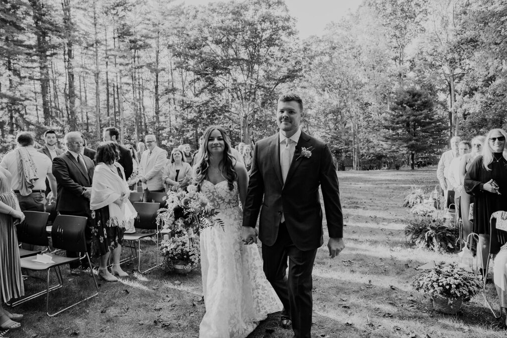 A bride and groom walk down the aisle together on the way to their ceremony. They are holding hands