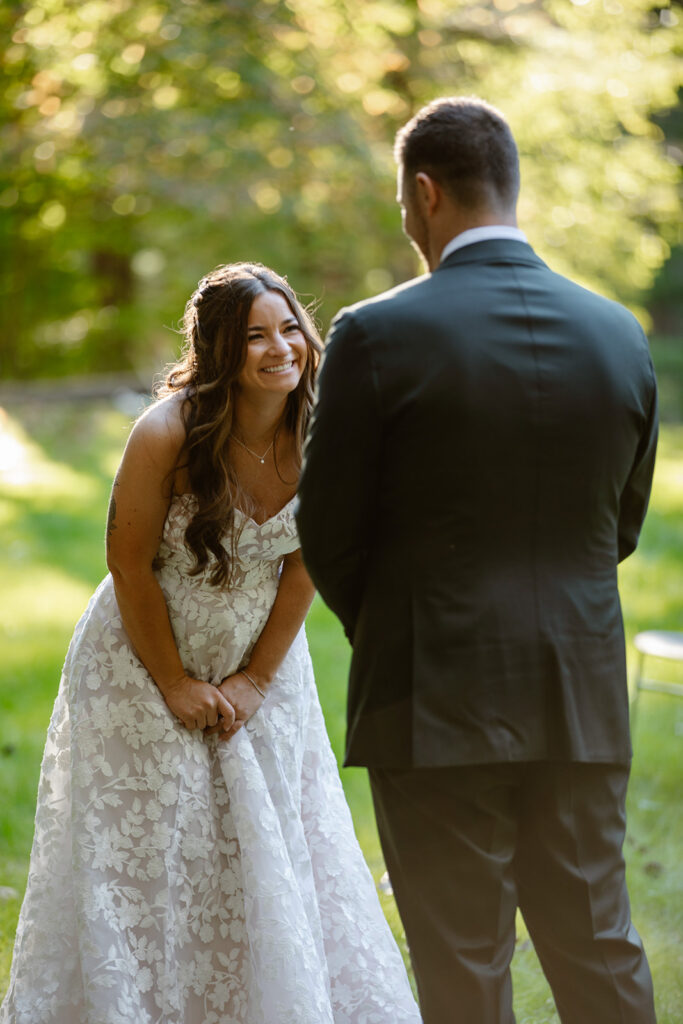 A bride is bent over laughing at her groom while he reads his personal vows