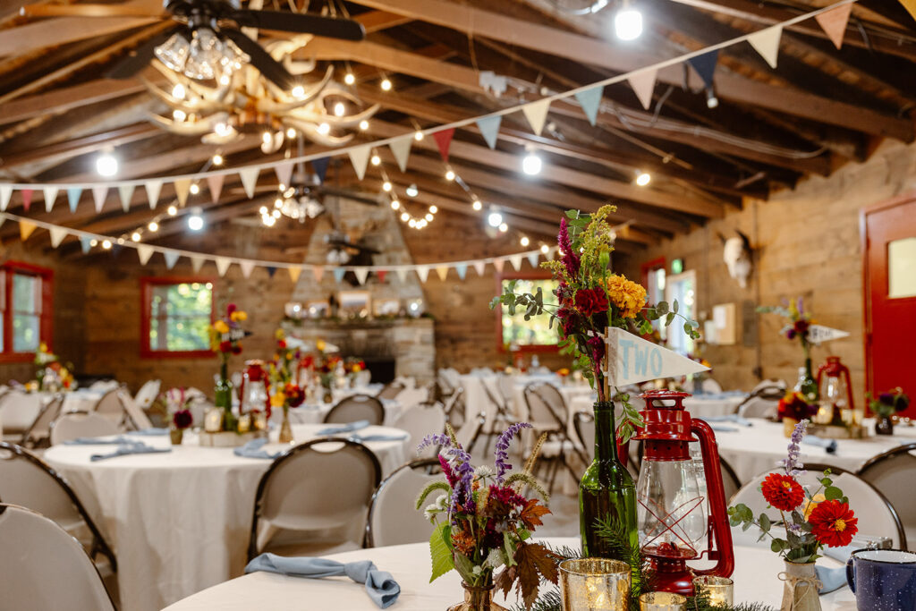 A summer camp lodge decorated for a wedding reception. There are red lanterns, flowers, bunting, and penants. 