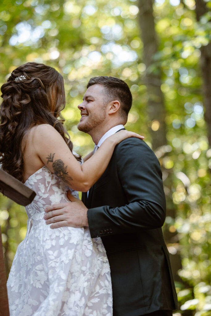 A bride and groom see each other for the first time on their wedding day. They are standing with their arms around each other, and the groom is smiling