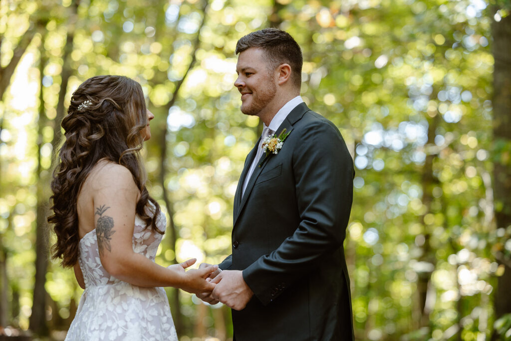 A bride and groom look at one another for the first time on their wedding day. They are in the woods, and smiling