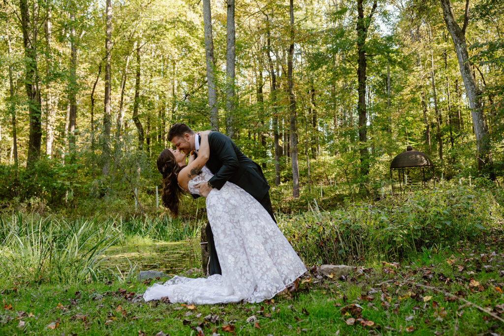 A groom dips his bride in the woods on their wedding day. 