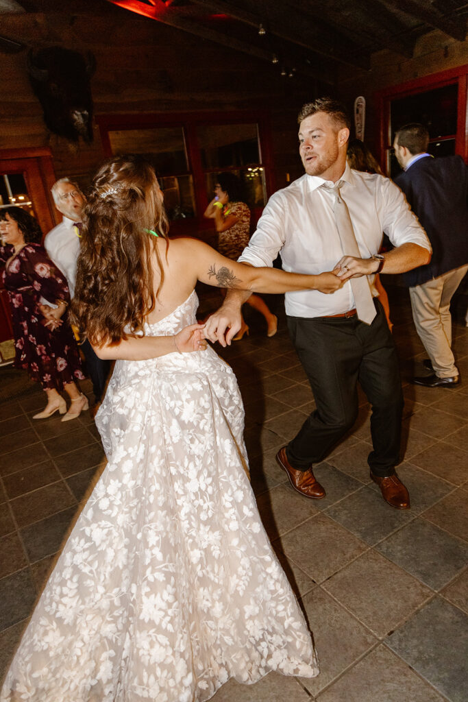 A bride and groom are dancing on their wedding day. Their arms are crossed like the groom is about to spin the bride. She is wearing a gorgeous lace dress