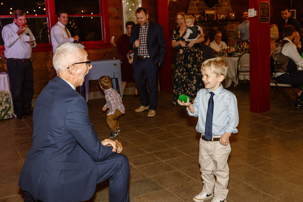 The bride's father performs magic for the kids at the wedding. He has a green foam ball that he makes disappear, and then reappear in the hand of a kid