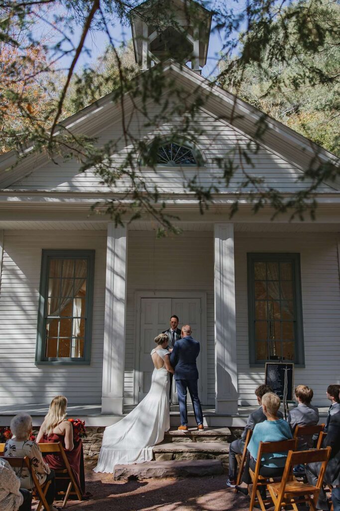 A bride and groom stand in front of the chapel at Hickory Run State Park during their elopement with family