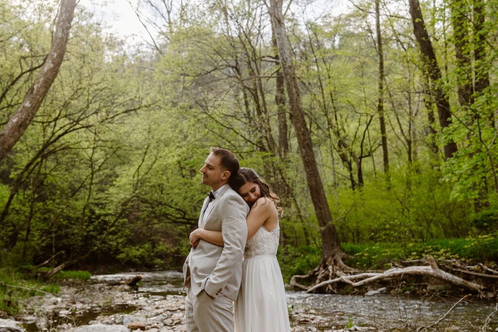 A bride snuggles behind her groom on their wedding day by a waterfall in Pennsylvania