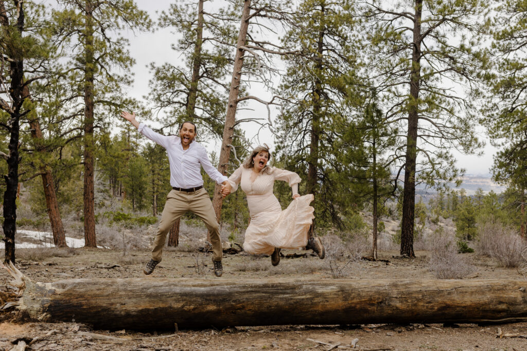 a couple jumping in the air over a log in the woods. Elopement Checklist