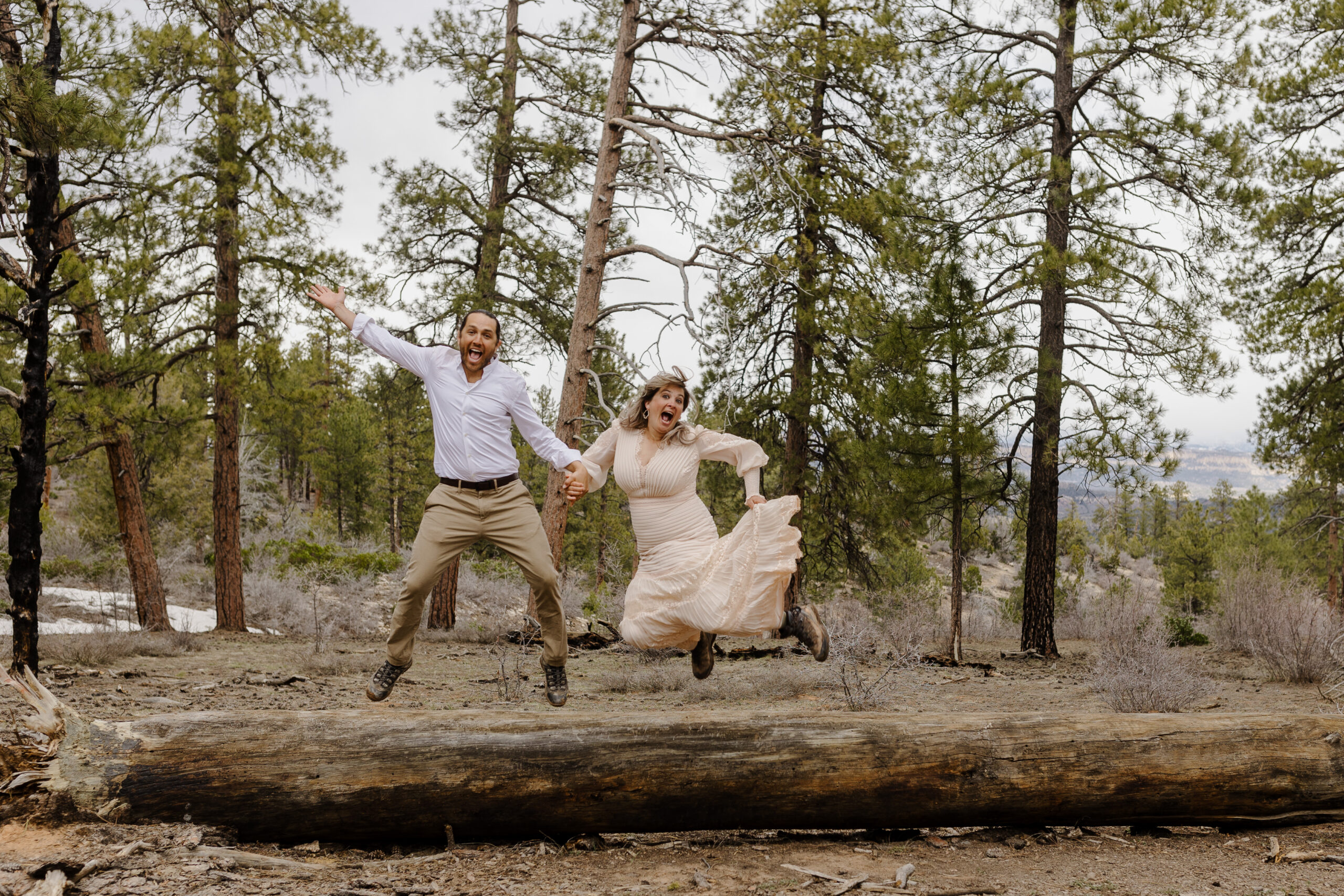 a couple jumping in the air over a log in the woods