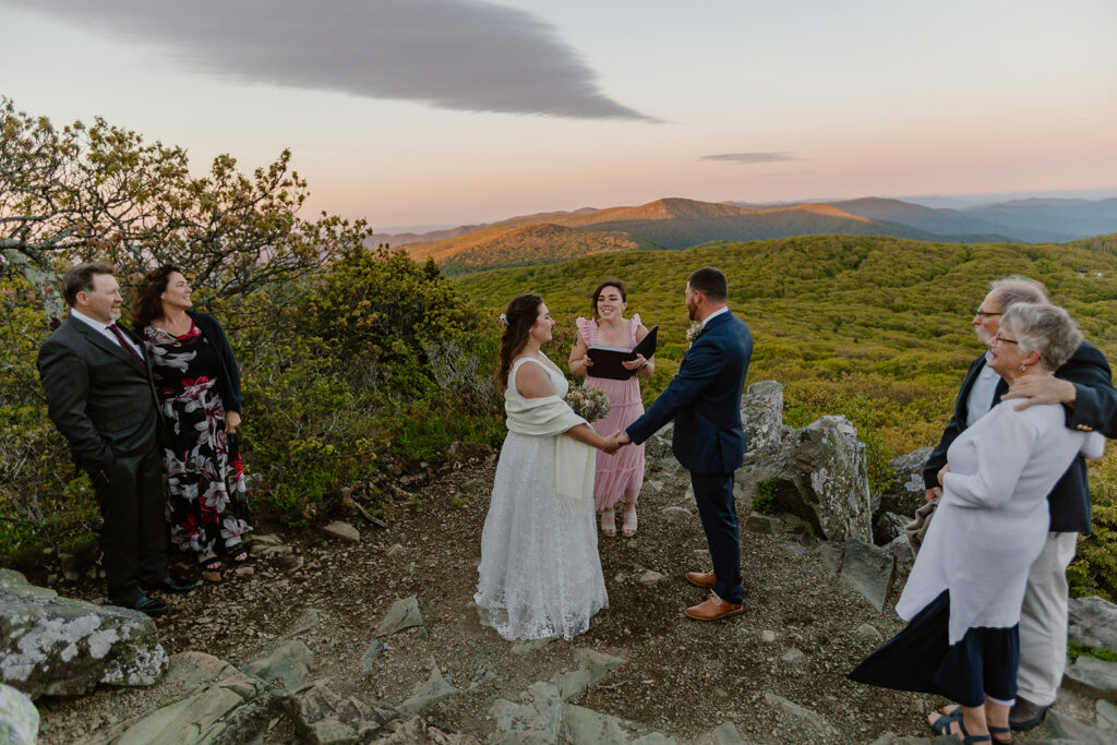 A couple during their ceremony at Stony Man Summit. They are holding hands, and the sun is rising.