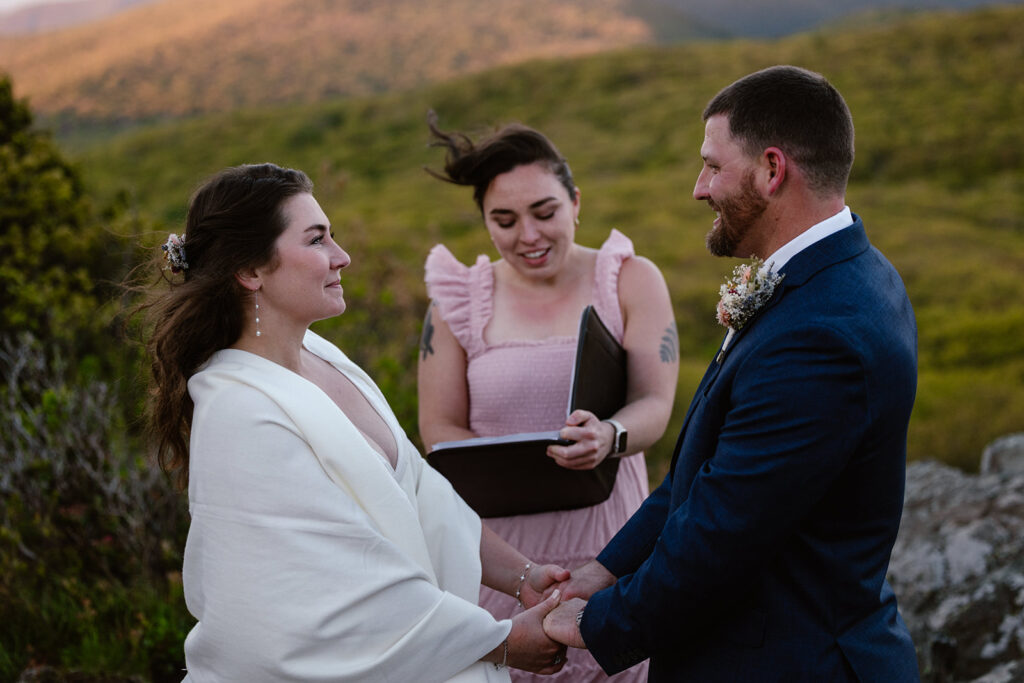 A bride and groom holding hands and smiling at one another during their sunrise hiking elopement