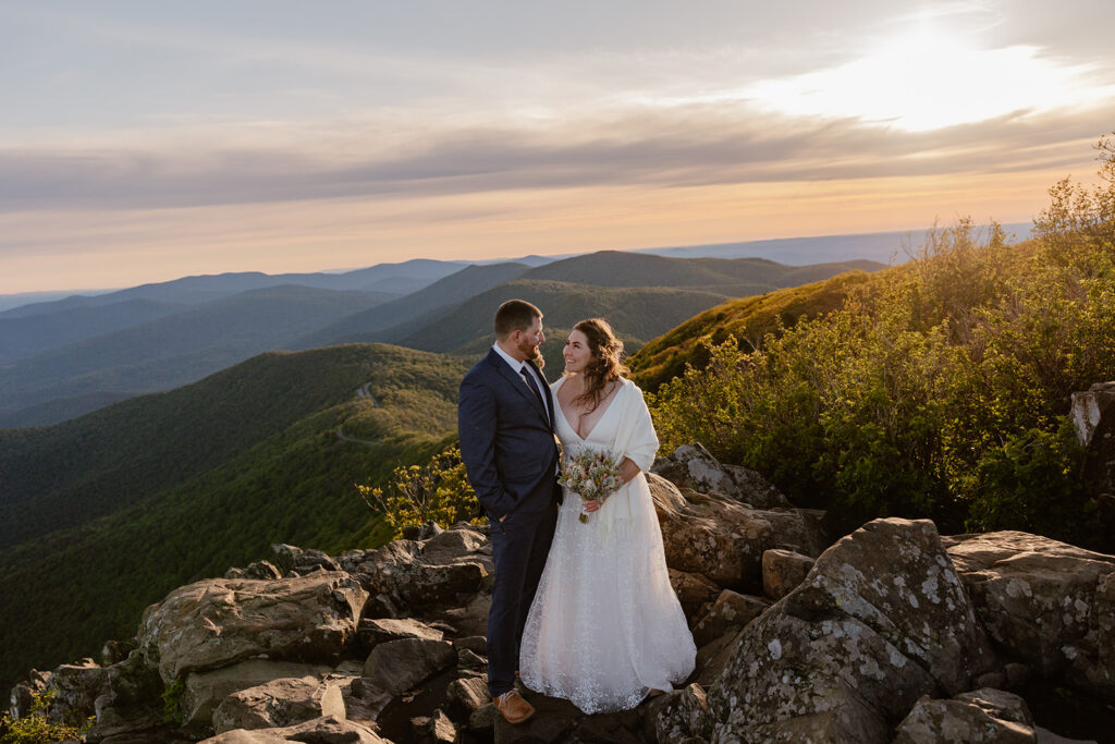 A bride and groom stand at Stony Man smiling at one another while the sunrises