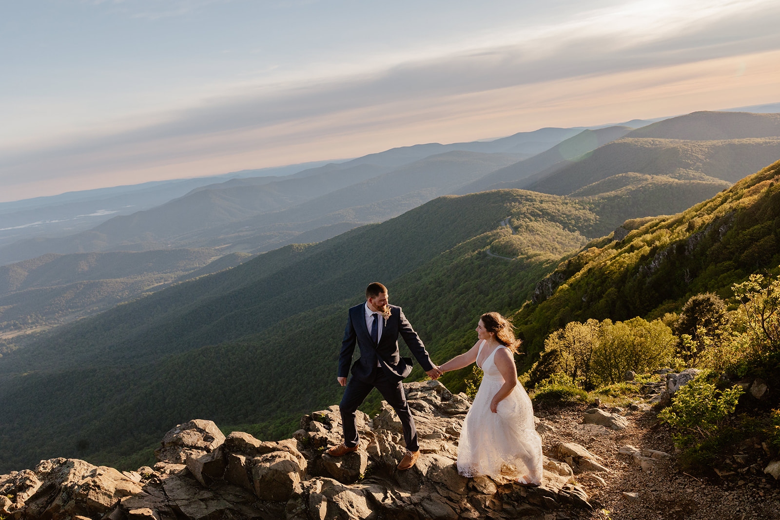 A bride and groom holding hands walk across mountains during their wedding in Shenandoah National Park