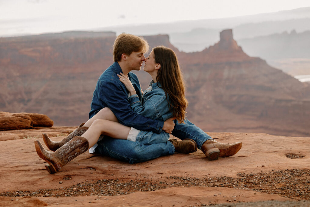 A couple sit interlocked at Dead Horse Point while the sunrises