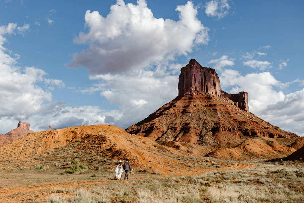 A couple walks towards a red rock formation in Moab on their elopement day