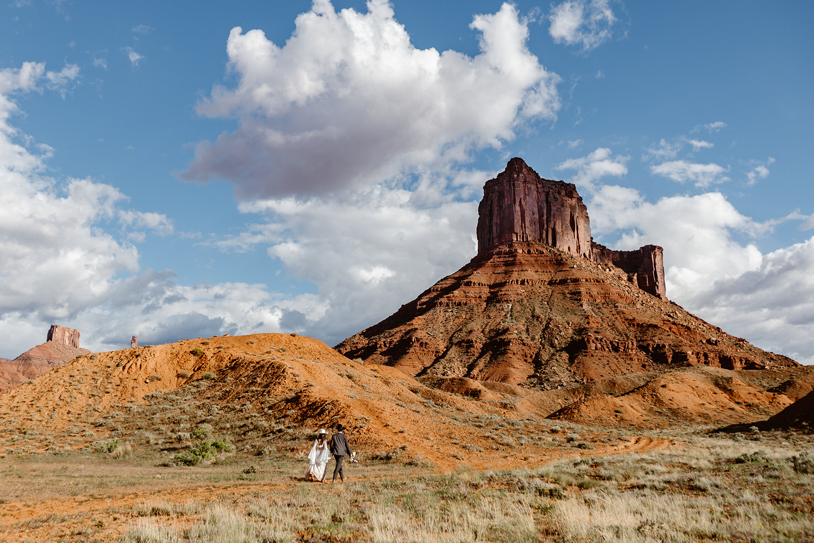 A couple walks towards a red rock formation in Moab on their elopement day