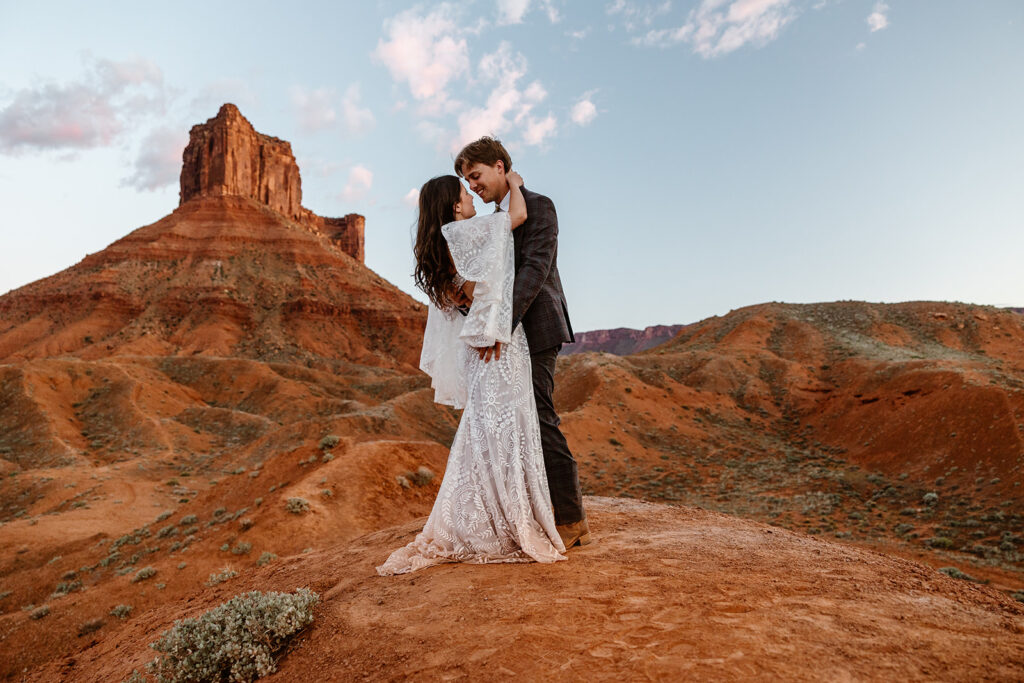 A bride and groom standing close during their elopement day. She is wearing a beautiful boho dress. They are standing in front of some massive red rocks.