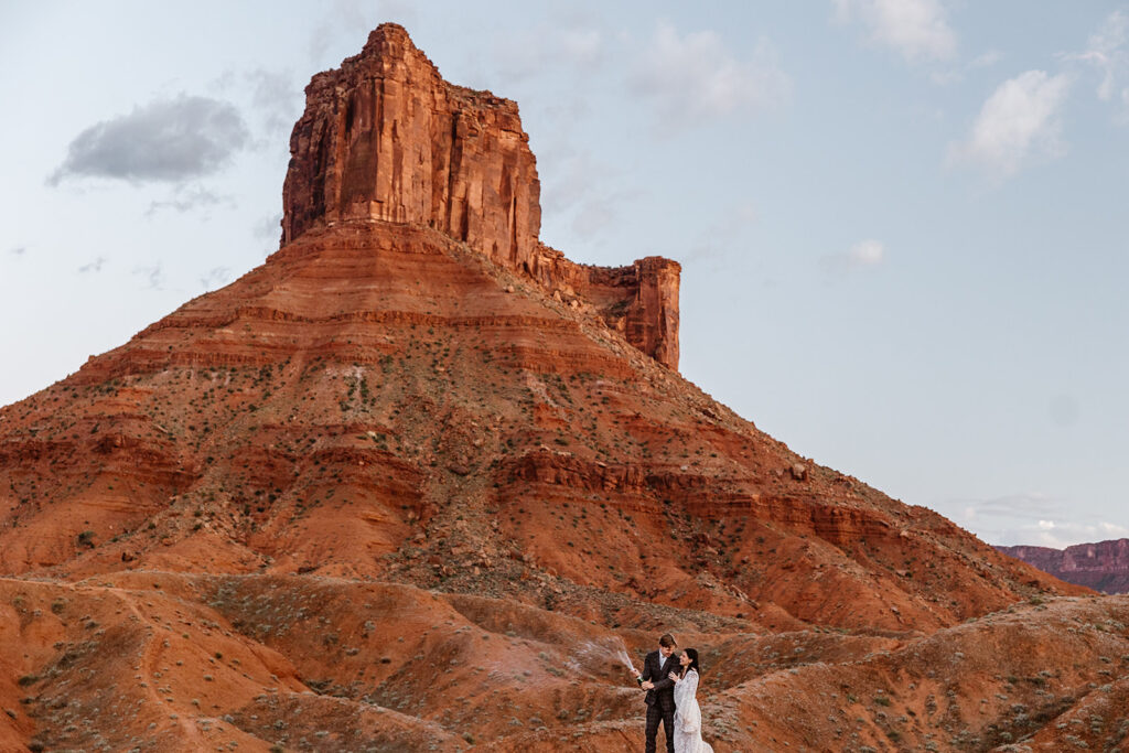A bride and groom pop Champagne to celebrate their elopement in front of the Red Rock formations of Ida Gulch