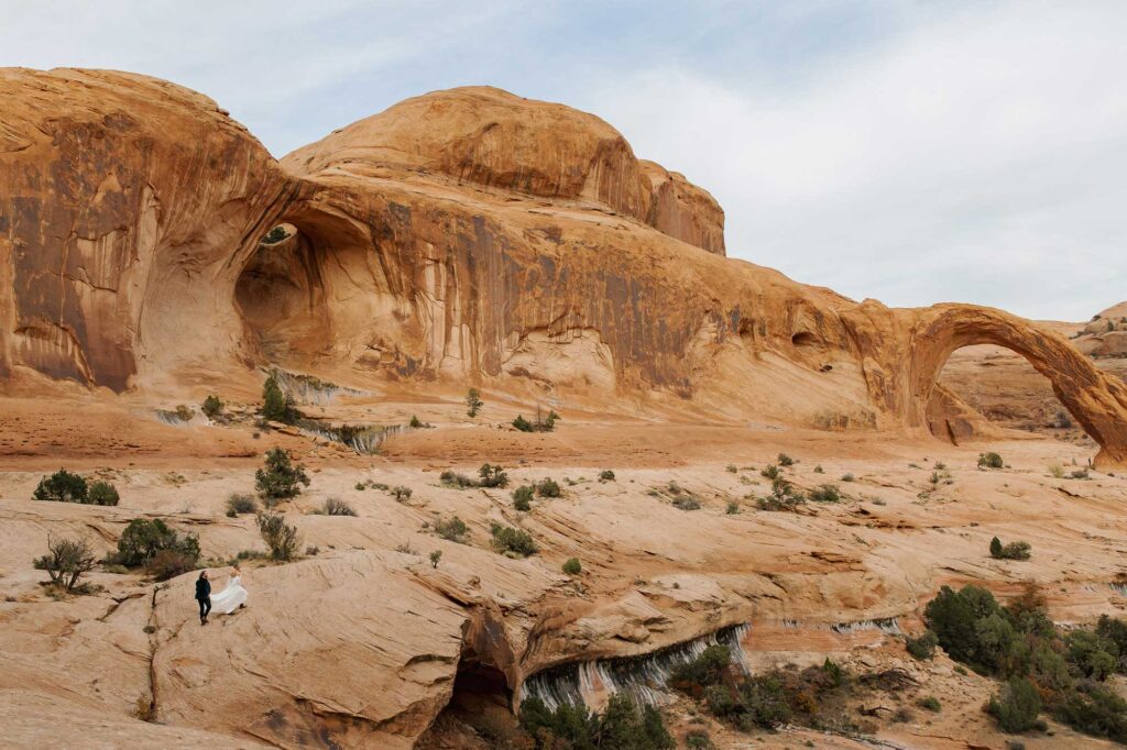 A groom holds his brides dress as they walk towards Corona Arch in Moab for their elopement ceremony. 