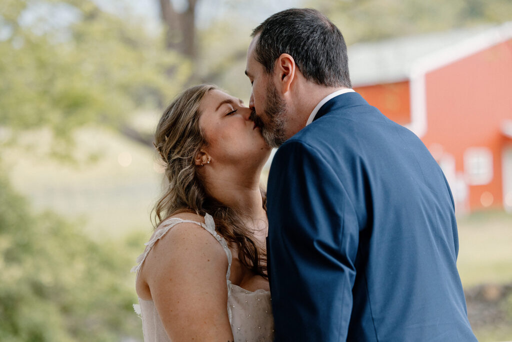 A bride and groom kiss on their wedding day after seeing each other for the first time. The groom is wearing a blue suit, and the bride is wearing a lace dress