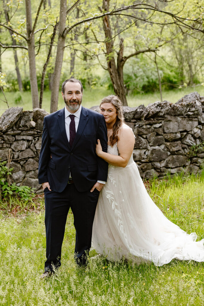 A bride and groom standing in front of a stone wall at their AirBNB in Luray Virginia before their micro wedding  ceremony.