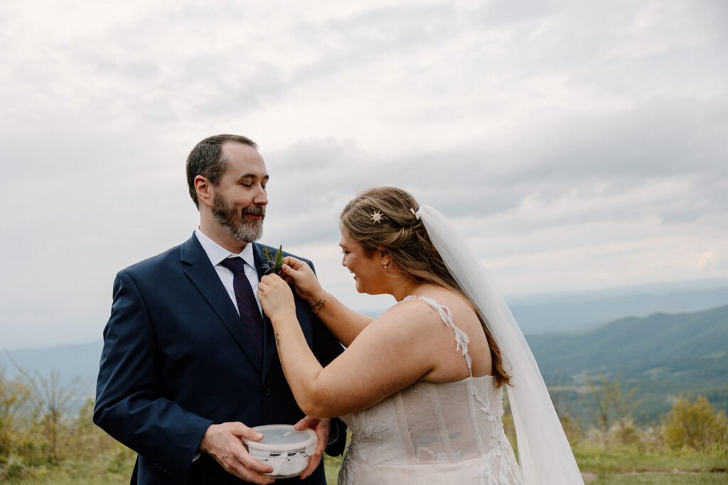 A bride pins a boutonniere on her groom on her wedding day right before their ceremony at Jewell Hollow in Shenandoah