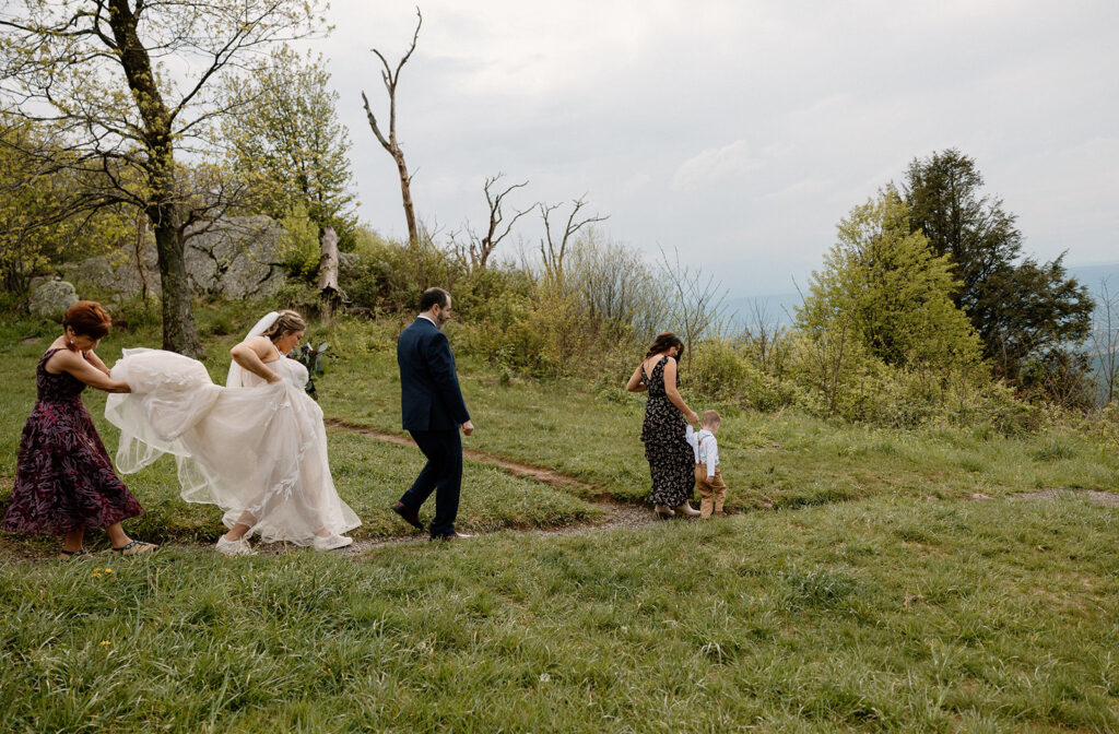 A bride's mom holds up the brides dress while they walk to the ceremony spot at Jewell Hollow in Shenandoah. The groom, the sister of the bride, and their nephew are also walking on the trail