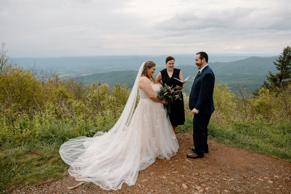 A bride and groom stand at an overlook in Virginia with an officiant on their wedding day.