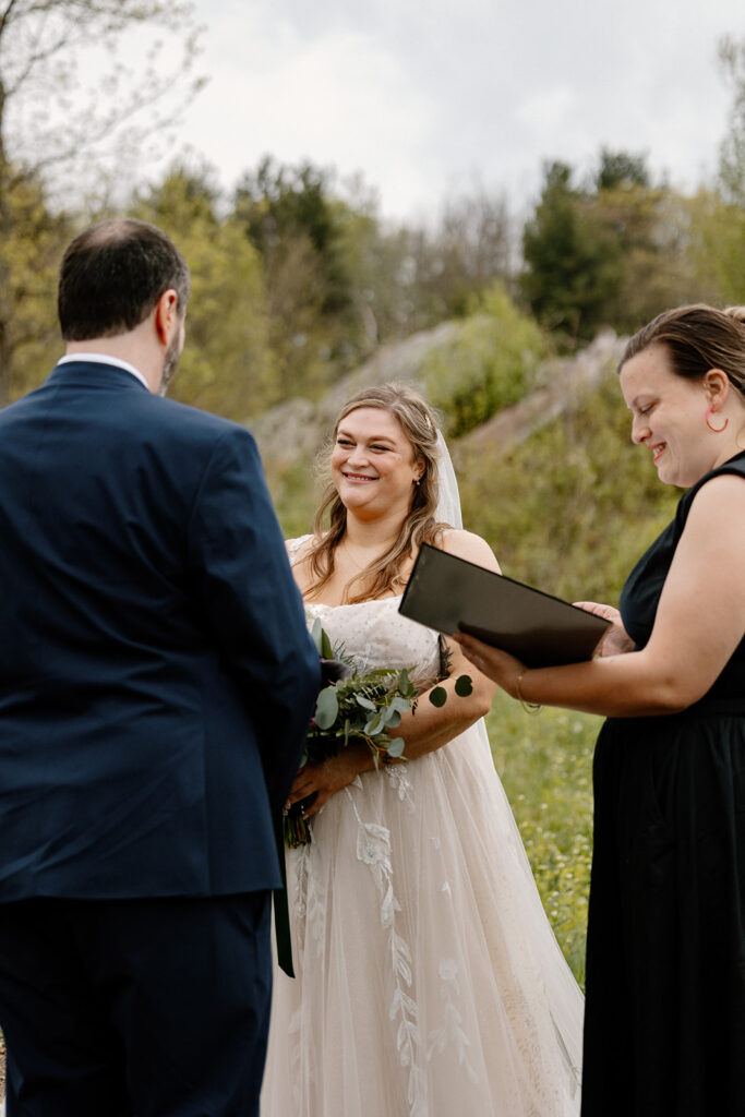 A bride smiles as her groom says his vows. 