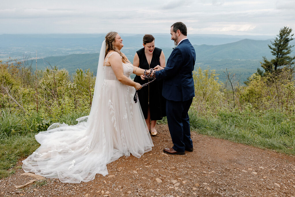 A bride and groom laugh during their handfasting ceremony with an officiant in virginia