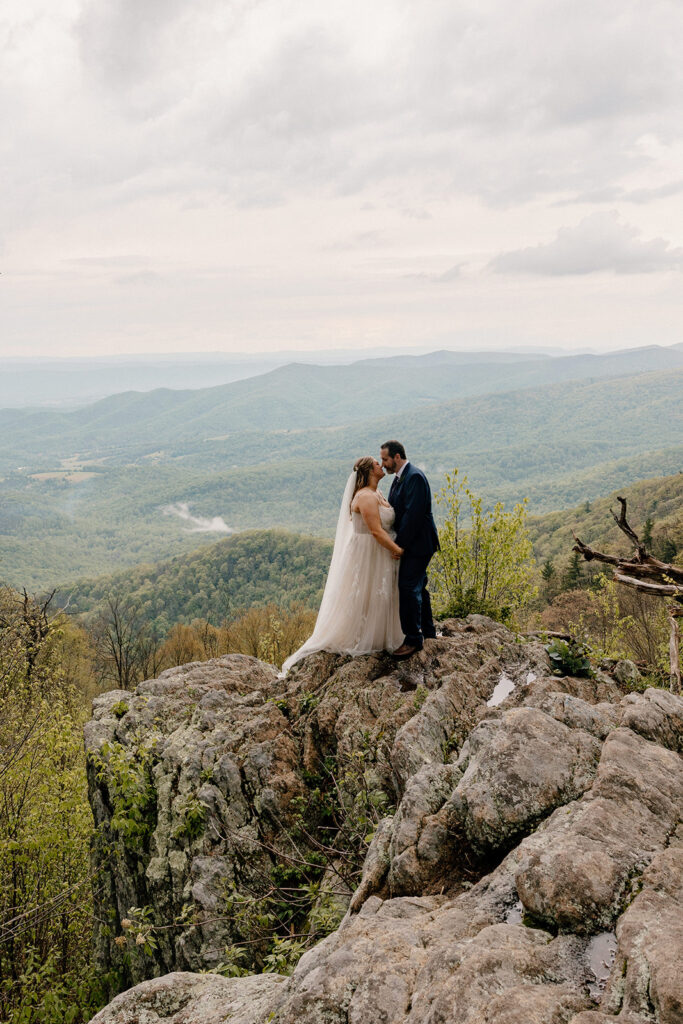 A bride and groom atop rocks at Jewell Hollow. You can see a view of the Blue Ridge Mountains in the background.