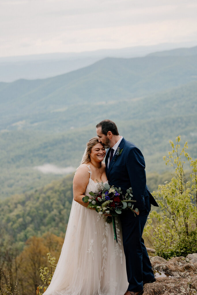A groom kisses a brides forehead at an overlook in Shenandoah