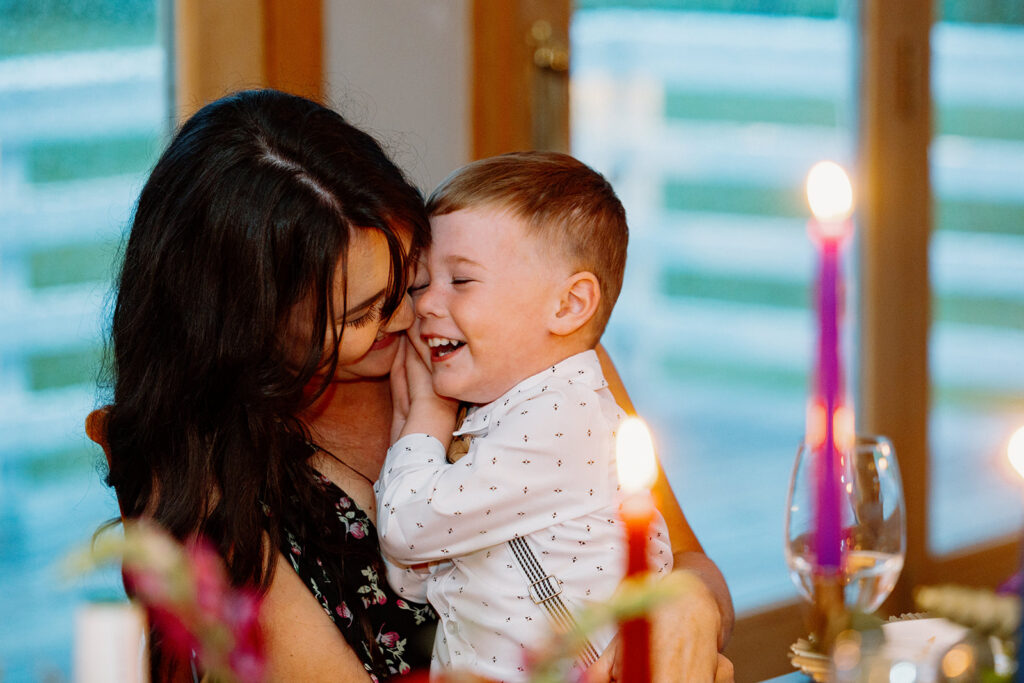 A child sits on his moms laps, and laughs during the wedding reception.