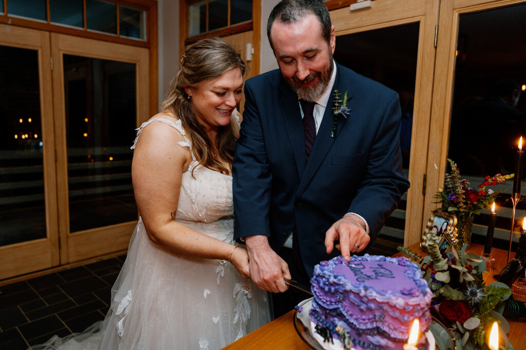 The bride and groom cutting the cake. The groom is taking a finger full of icing as he is cutting