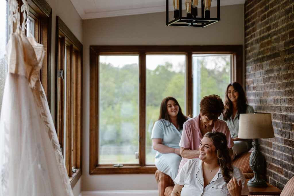 A bride, her sisters and mom, get ready at an Airbnb in Luray Virginia on the day of their micro wedding. They are all in pajamas, and the dress in hanging in the foreground.