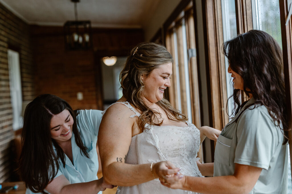 Sisters helping their sister who is the bride get her dress on. They are getting ready to have a micro wedding in Virginia