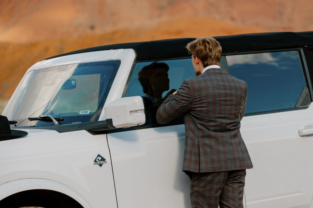 A groom straightens his bolo using the reflection of his car window on his elopement day.