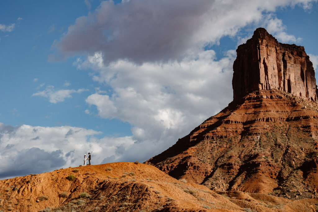 A photo of one of Moab's epic landscapes featuring a couple on a hill eloping.