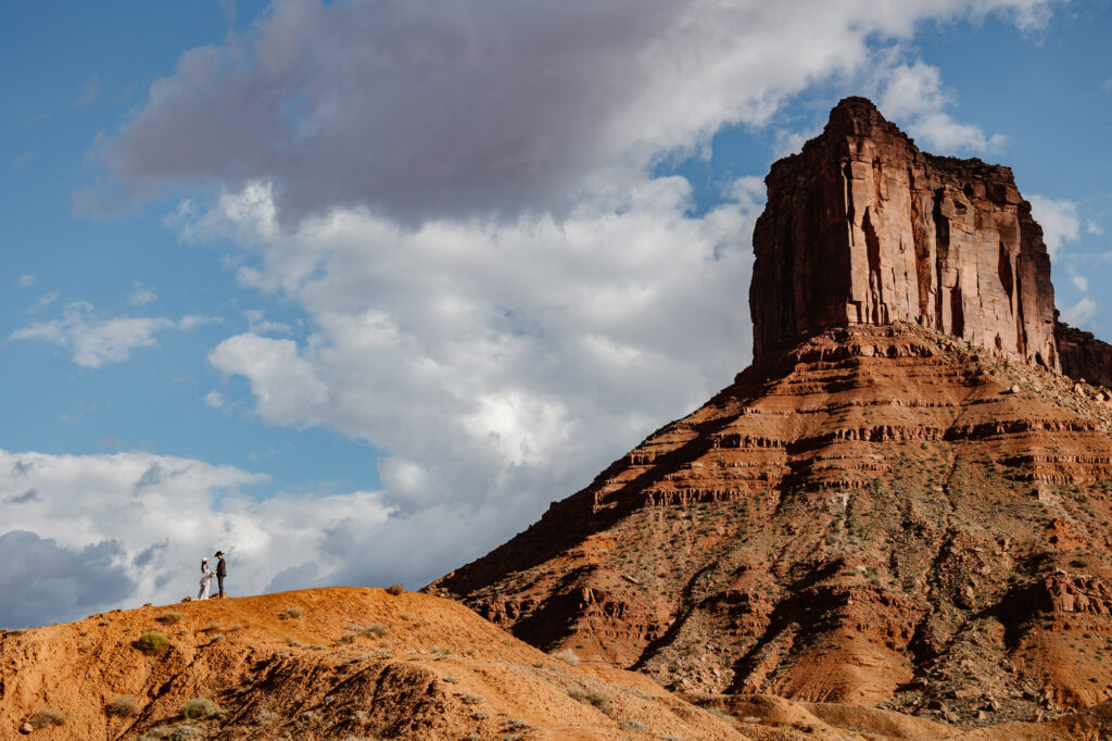 A photo of one of Moab's epic landscapes featuring a couple on a hill eloping.