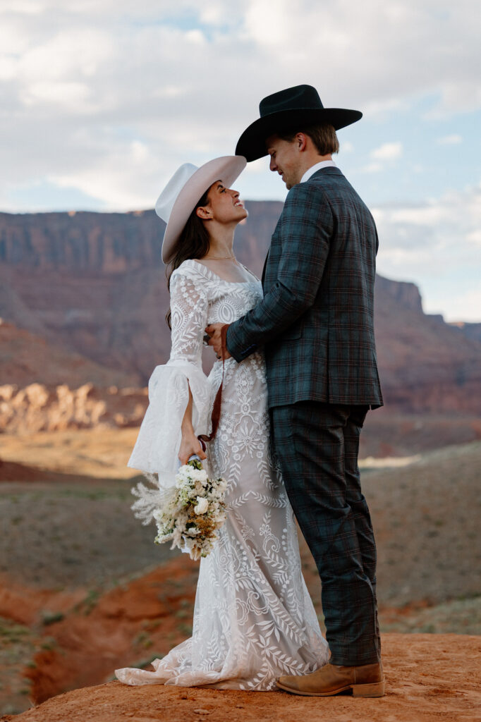 A bride and groom wearing cowboy hats look at one another lovingly during their elopement day in Utah