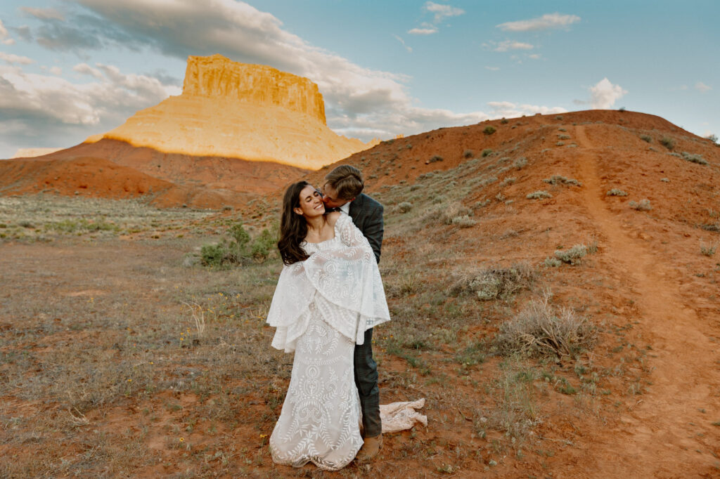 A groom kisses the neck of his bride playfully in Moab Utah