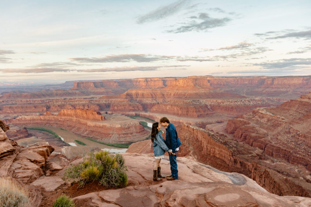 A bride and groom stand facing each other in front of Dead Horse Point during a sunrise session on their elopement day.
