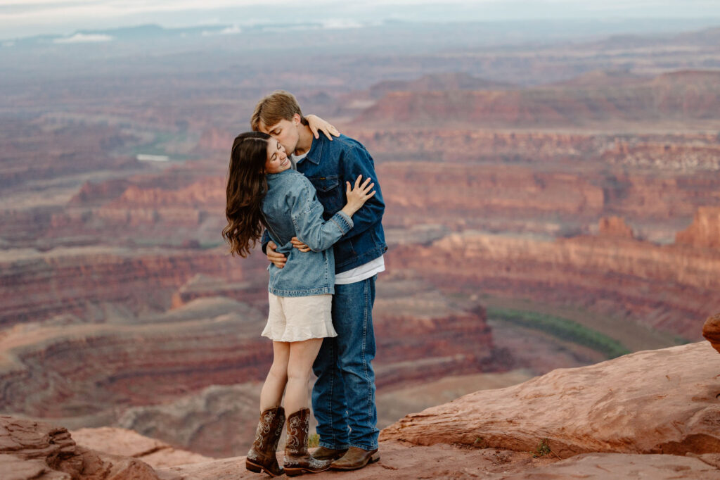 A groom kisses his brides cheek in front of Dead Horse Point in Moab. The couple chose to do a sunrise session here before their sunset vows at Ida Gulch