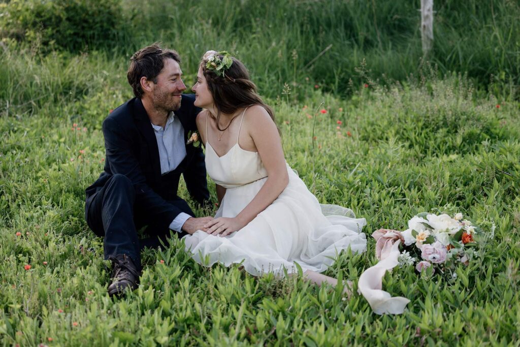 A couple sits in a patch of grass and wild poppies looking at one another lovingly. how to legally get married in pennsylvania