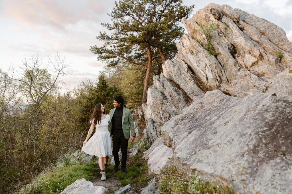 A bride and groom walking on their elopement day. They are walking by some cool rock formations in the Virginia Mountains. 